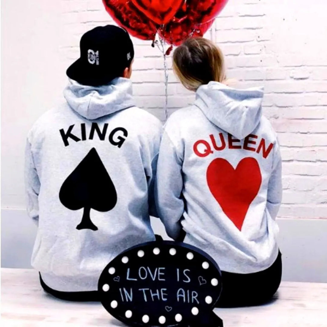 Matching light gray couple hoodies from CouplesChoices.com with bold back prints — “KING” with a black spade and “QUEEN” with a red heart. A playful and eye-catching set for couples who celebrate love with personality and style.